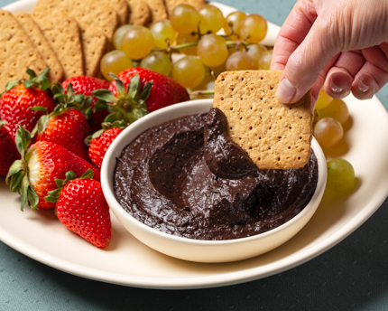 Bol de houmous au chocolat sur un plateau avec des biscuits Graham, des fraises et des raisins