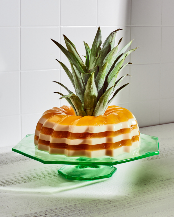 Gelée anglaise au piña colada sur un support en verre vert présenté décoré d'une tête d'ananas au milieu.