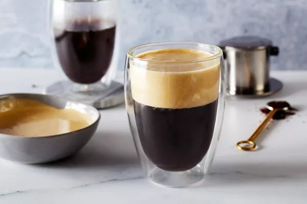 Un verre de café vietnamien à la mousse d'œuf avec un bol de mousse d'œuf, un verre de café et un équipement pour faire du café.