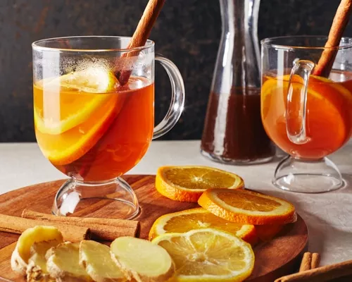 Deux grogs chauds dans des mugs en verre garnis de tranches d'orange, de bâtons de cannelle et de tranches de gingembre