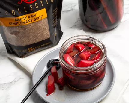 Conserve de rhubarbe marinée sur une assiette avec cuillère de service et un paquet de Sucre Turbinado Redpath™ Simplement Brut