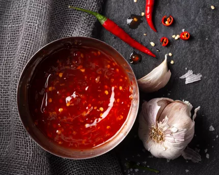 Sauce chili douce dans un bol en métal avec des piments chilis entiers, des piments émincés et une gousse d’ail